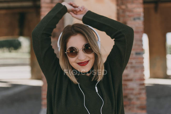 Дівчина в навушниках позує з піднятими руками — стокове фото