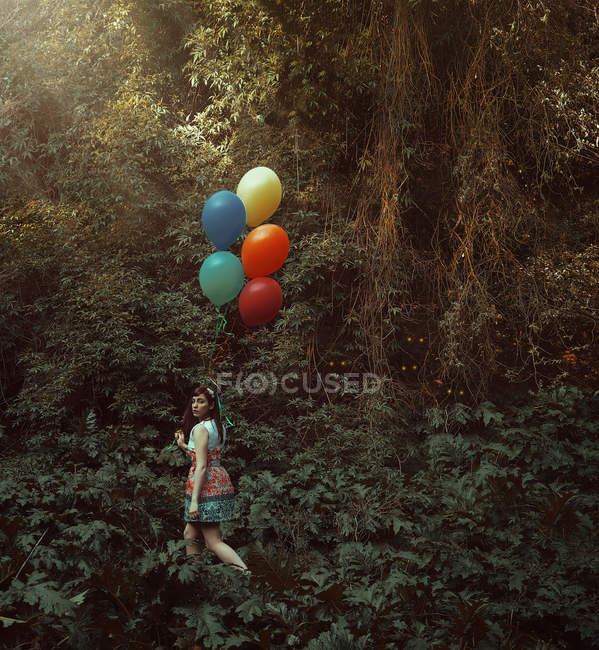 Jovem com balões coloridos caminhando na floresta silenciosa . — Fotografia de Stock