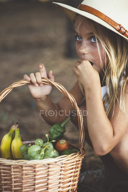 Niedliches Kind isst Obst aus Korb und schaut zur Seite — Stockfoto