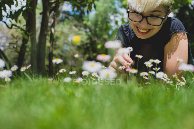 Щаслива дівчина з коротким волоссям лежить на траві і дивиться на квіти — стокове фото