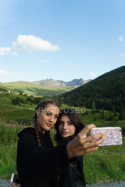 Les jeunes femmes debout sur la prairie ensemble et prendre selfie avec smartphone . — Photo de stock
