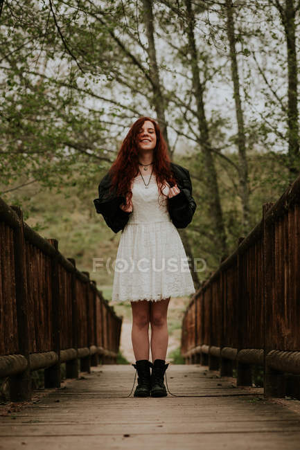 Menina alegre em vestido branco posando na ponte de madeira — Fotografia de Stock