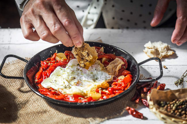 Vista de cerca de la mano poner ingrediente en la sartén con huevos revueltos y tomates secos - foto de stock