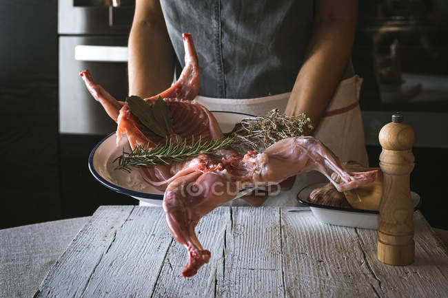 Close-up da mulher segurando carcaça de coelho cru com ingredientes na mesa de madeira — Fotografia de Stock