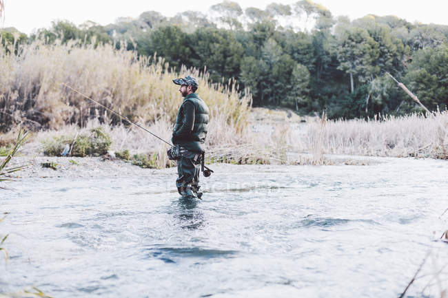 Vista lateral do homem de pé no rio e pesca com vara — Fotografia de Stock