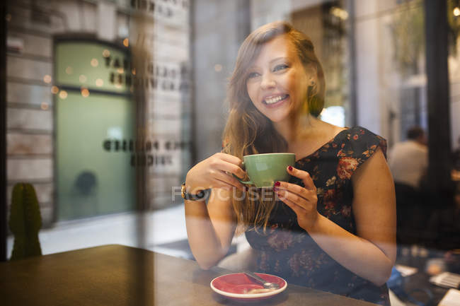 Вид через вікно на жінку, маючи каву на самоті в кафетерії — стокове фото
