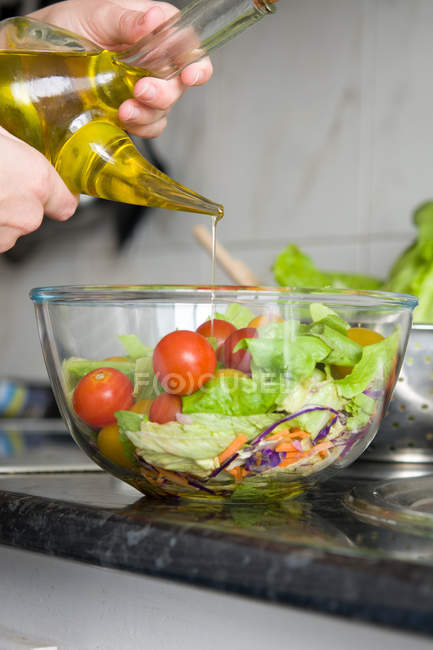 Manos de cultivo añadiendo aceite de oliva a un bol de ensalada - foto de stock