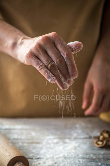 Крупним планом вид руки, що поливає борошно на дерев'яний стіл — стокове фото