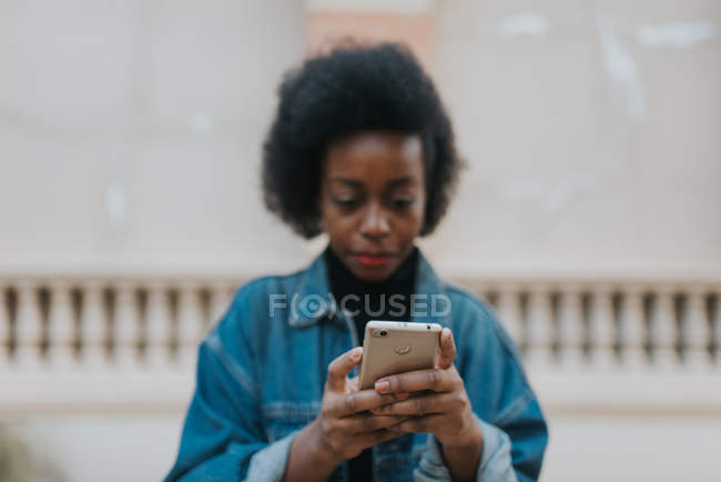 Close up view of smartphone in hands of young woman wearing denim coat at street scene — Stock Photo