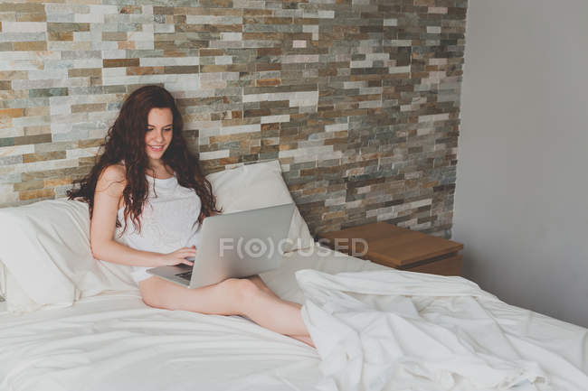 Женщина отдыхает в постели и с помощью ноутбука — стоковое фото