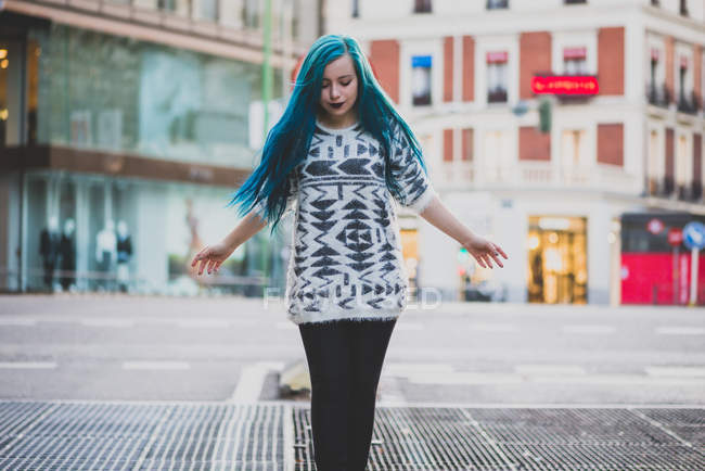 Портрет синьоволохатої дівчини, що йде з жестом відкритими руками і дивиться вниз на міську сцену — стокове фото