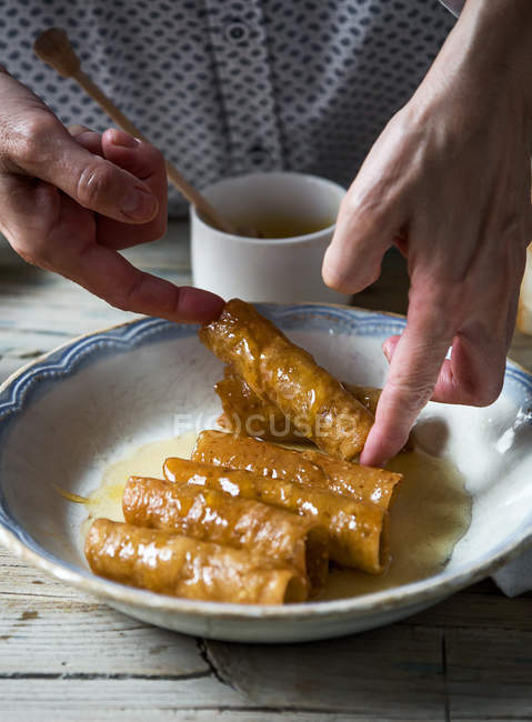 Crop image of hands taking fried honey dough tubes from plate — Stock Photo