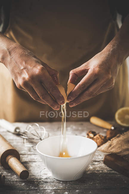 Seção média de ovo rachaduras feminino na tigela em mesa de madeira com utensílios de cozinha — Fotografia de Stock