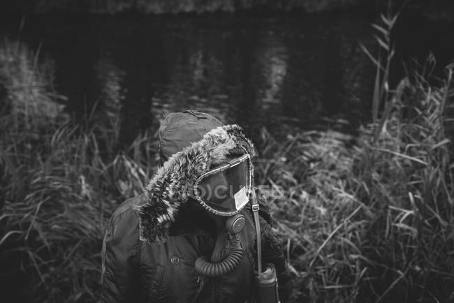 Vue grand angle du manteau masculin et du masque à gaz debout près de l'étang — Photo de stock
