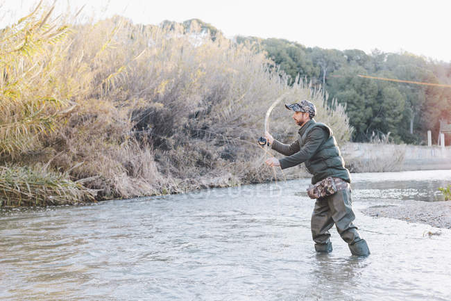 Fisher uomo in piedi nel fiume e la pesca con canna — Foto stock