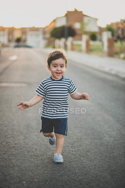 Cute boy in shorts running happily towards camera on road. — Stock Photo
