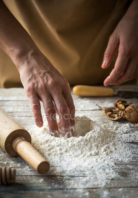 Vista da vicino delle mani femminili che fanno cratere in mucchio di farina — Foto stock