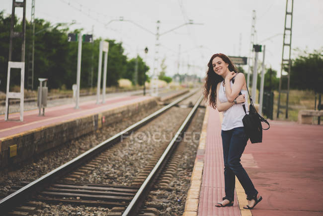Retrato de menina de cabelos vermelhos sorridentes na plataforma ferroviária olhando para fora para o trem — Fotografia de Stock