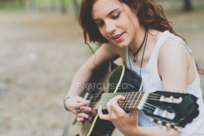 Retrato de menina sardenta sorridente com cabelo vermelho tocando guitarra na floresta — Fotografia de Stock