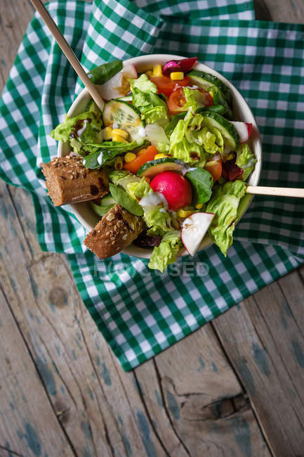 Frischer Gemüsesalat in Schüssel mit Brot auf Stoff auf Holzoberfläche — Stockfoto