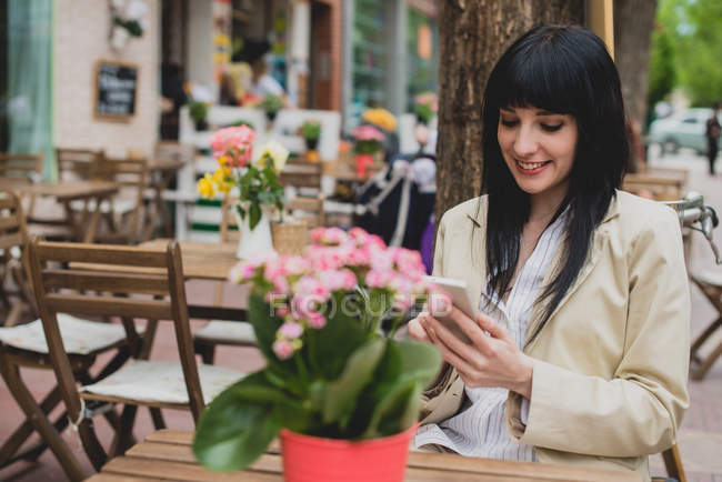 Brunette femme utilisant smartphone café terrasse table — Photo de stock