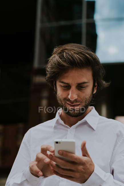 Портрет брюнетки бизнесмена в белой рубашке с использованием смартфона на городской сцене — стоковое фото