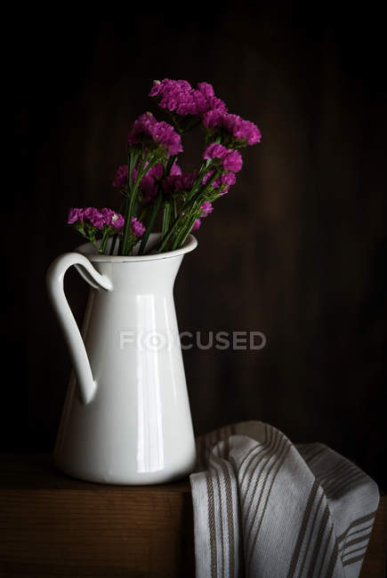 Fresh purple carnations in mug on dark background with kitchen towel — Stock Photo