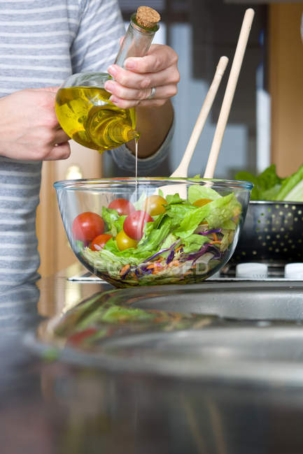 Женщина с урожая добавляет оливковое масло в миску салата — стоковое фото