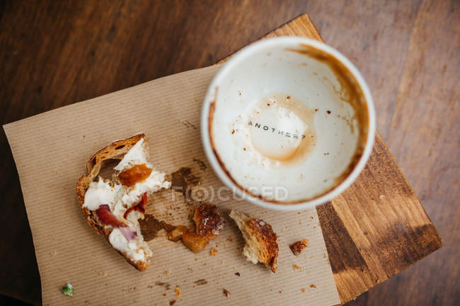 Draufsicht auf schmutzigen Becher mit Aufschrift unten und Resten von Toast mit Früchten und Sahne auf Holzbrett — Stockfoto