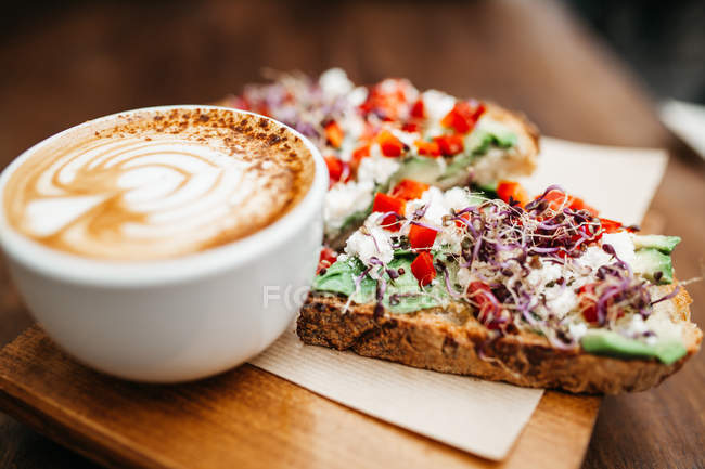 Close up view of cup of cappuccino and toasts with cream vegetables on wooden board — Stock Photo