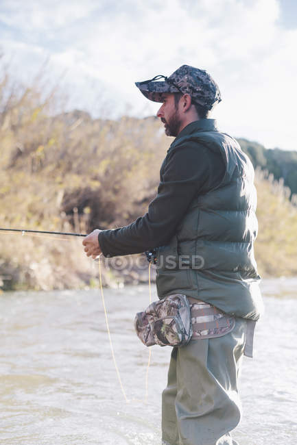 Seitenansicht eines Mannes, der am Fluss steht und mit der Rute fischt — Stockfoto