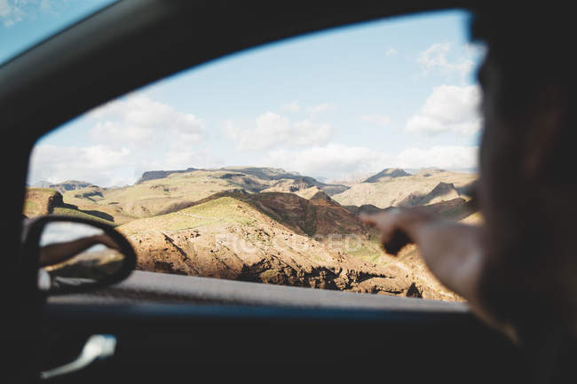 Crop man pointing out of car window to mountain landscape. — Stock Photo