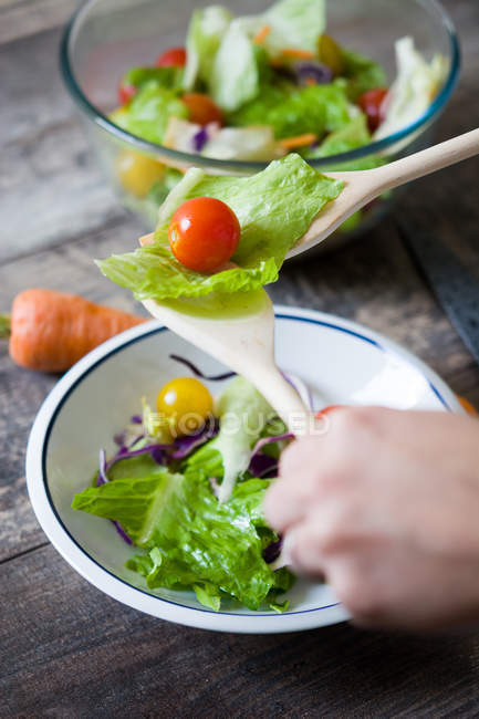 Mãos de colheita segurando legumes em colheres de salada sobre tigela — Fotografia de Stock
