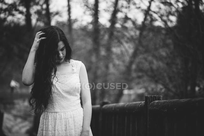 Sensual girl in white dress looking down and touching hair at nature — Stock Photo