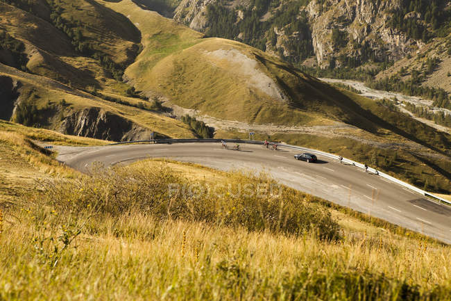 Отдаленный вид на горную дорогу с группой велосипедистов, опережающих транспортное средство в солнечный день — стоковое фото