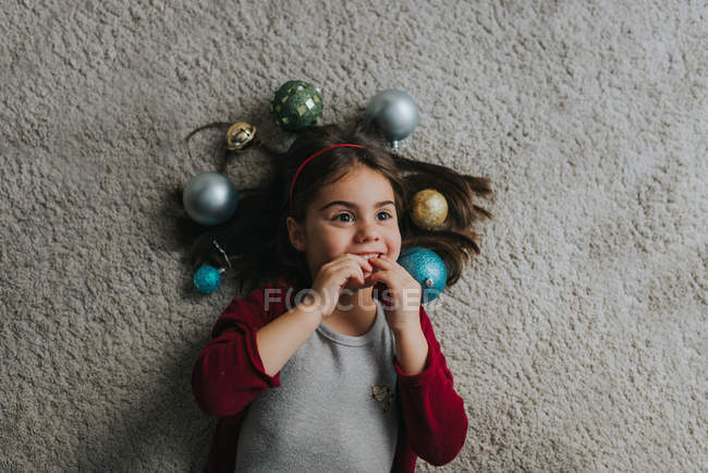 Sopra la vista della ragazza sdraiata sul pavimento del tappeto con le bagattelle di Natale intorno alla testa — Foto stock