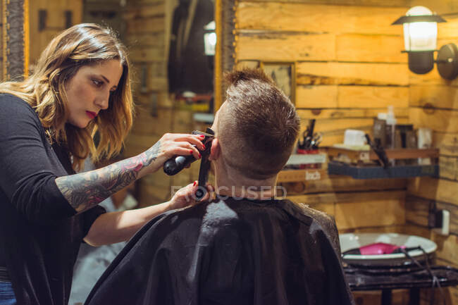 Uma mulher na loja fazendo um penteado elegante para uma pessoa irreconhecível. Horizontal dentro de casa tiro. — Fotografia de Stock