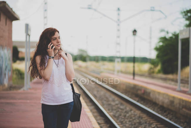 Retrato de menina com cabelo vermelho falando sobre smartphone na plataforma rural ferroviária — Fotografia de Stock