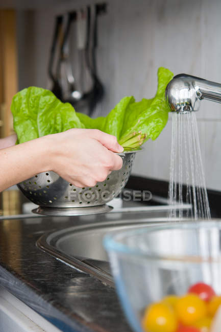 Крупным планом человеческих рук, моющих свежие листья салата в дуршлаге под краном — стоковое фото