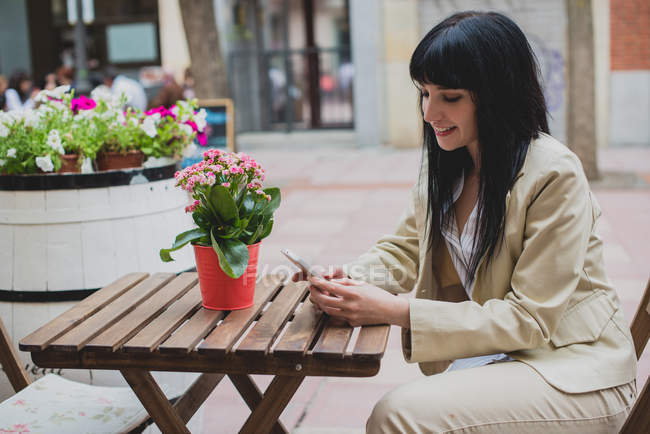 Bruna donna utilizzando smartphone caffè terrazza tavolo — Foto stock