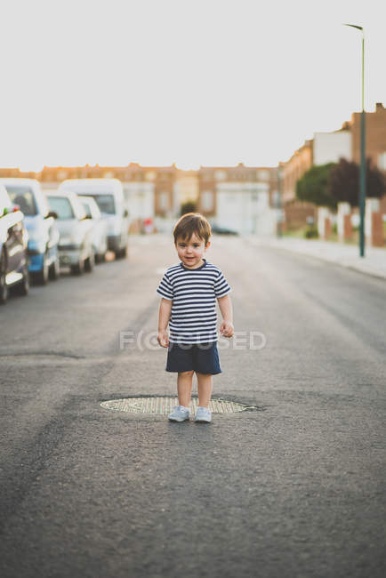 Boy posing at camera while standing on asphalt road in suburb — Stock Photo