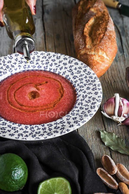 Томатный суп в узорной тарелке на деревянном столе с хлебом и ингредиентами — стоковое фото