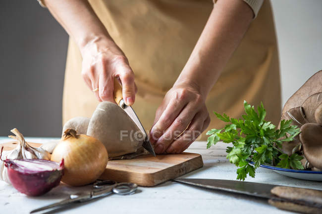 Середина жіночого нарізання грибів плевроту на дерев'яній дошці за столом з іншими інгредієнтами — стокове фото