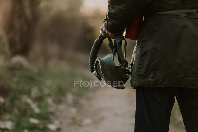 Cropped image of male holding gas mask in hand and walking on rural countryside road — Stock Photo