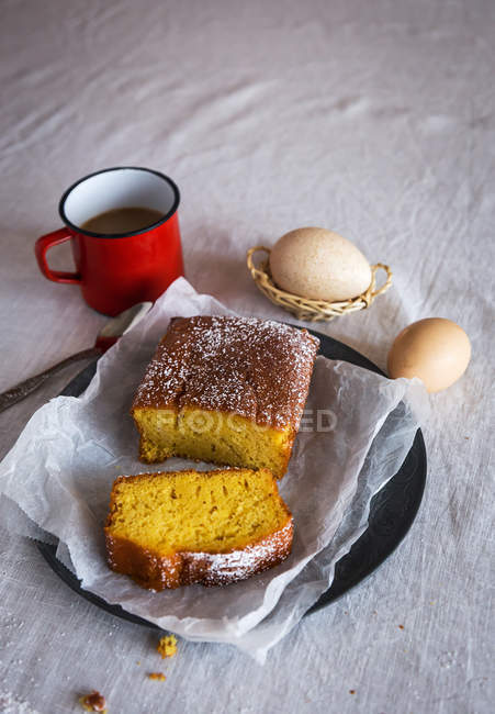 High angle view of homemade cake slices on plate over table with red mag and eggs on rumpled tablecloth — Stock Photo