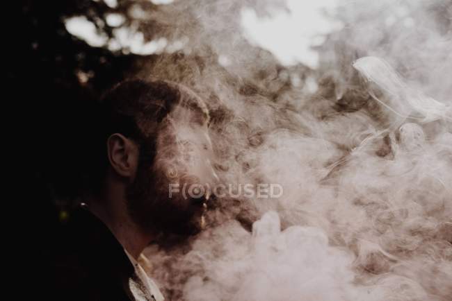 Vista laterale di uomo oscuro in piedi in fumo rosa tra i boschi — Foto stock