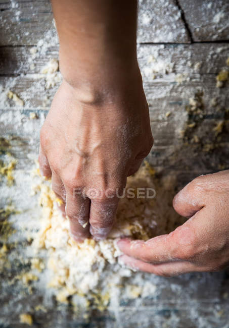 Acima de mãos amassando a massa de farinha sobre a mesa de madeira rural — Fotografia de Stock