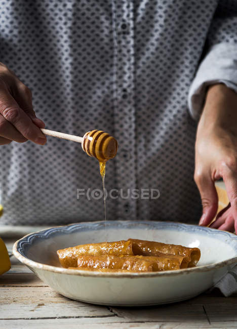 Close up view of female hand pouring honey on fried honey dough tubes with honey spoon — Stock Photo