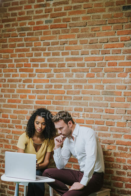 Thoughtful woman and man looking at notebook on the background of brick wall. Vertical indoors shot — Stock Photo