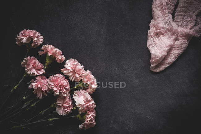 Fundo floral com cravos rosa e tecido de olhar na superfície de pedra preta — Fotografia de Stock